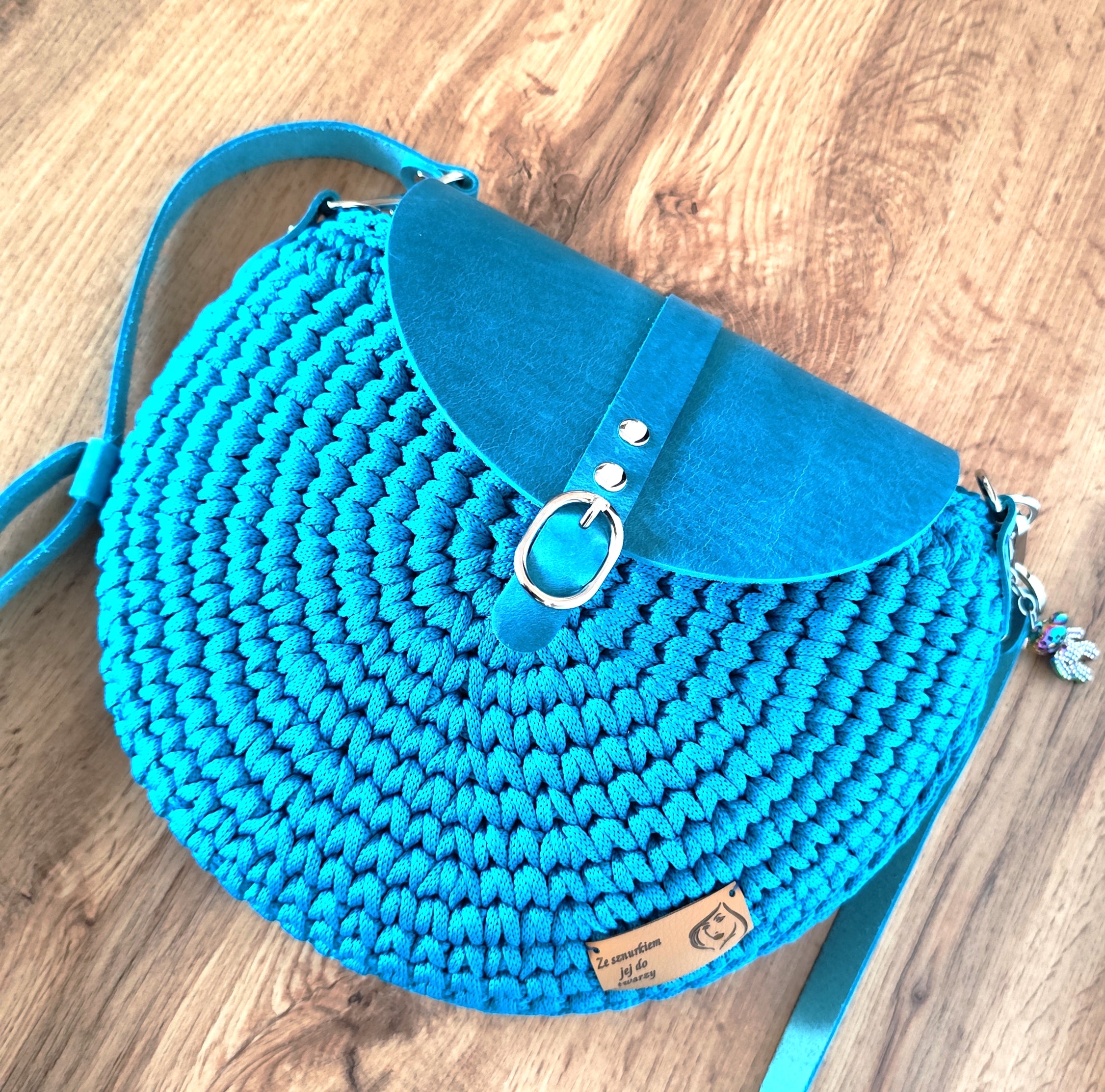 Okrągła torebka ze sznurka w kolorze turkusowym ze skórzaną klapką i srebrną klamrą